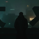 K, the Blade Runner, stands silhouetted against the city he's looking down on from a tall building.